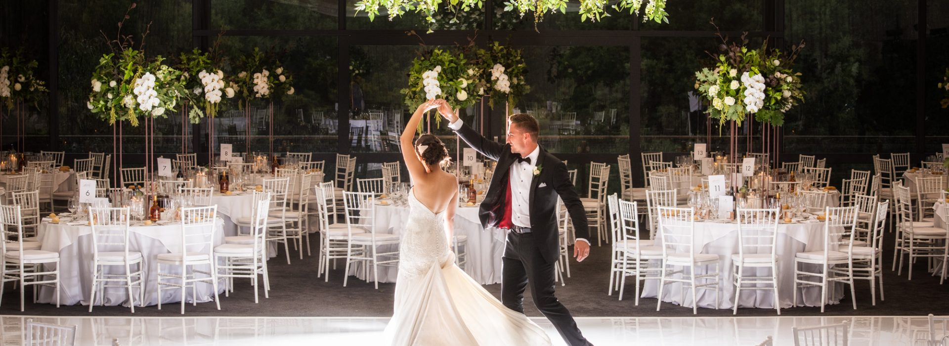 A beautiful bride and groom dancing in a grand room with elegant white chandeliers - a magical moment at a Melbourne wedding venue.